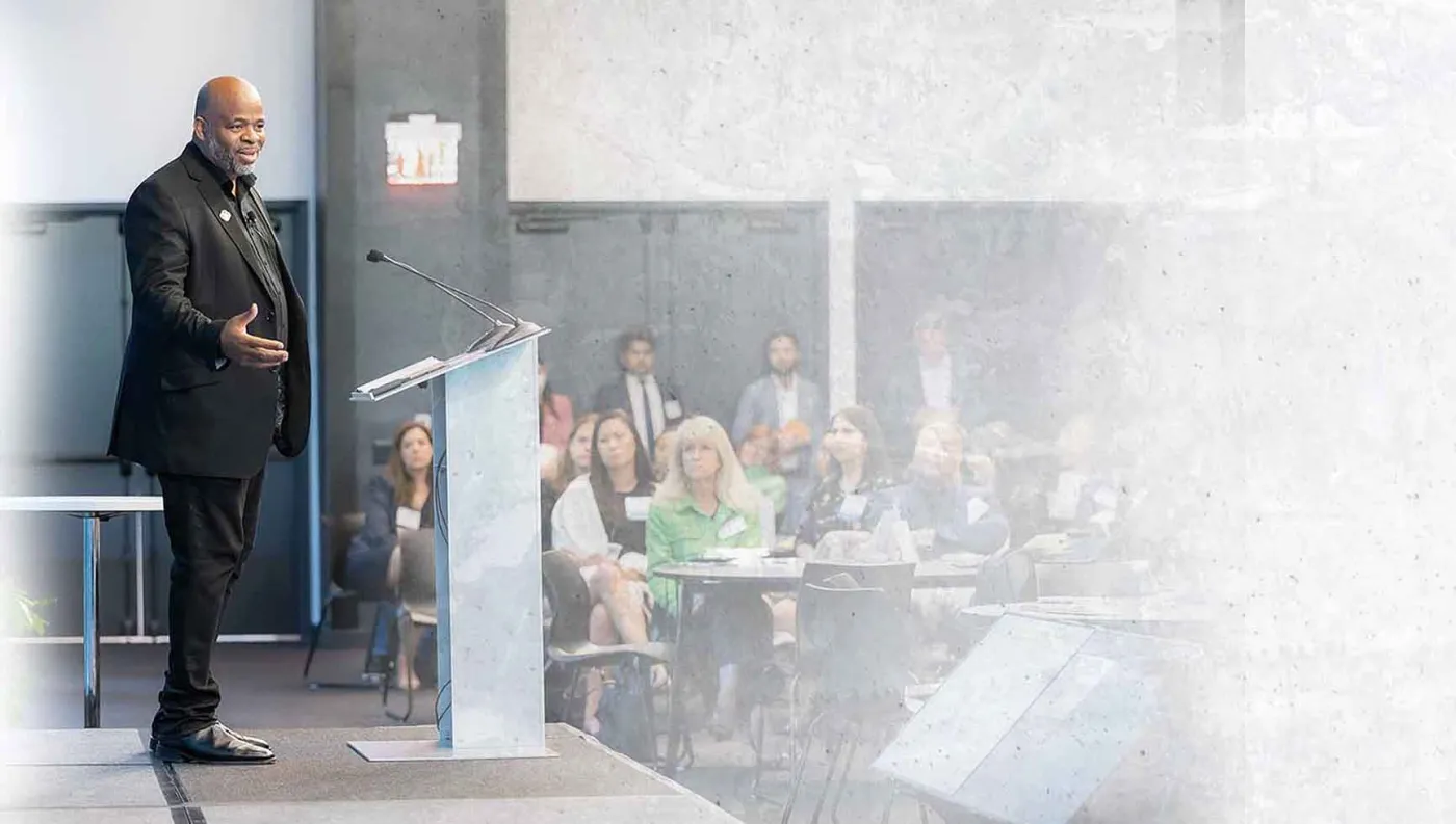 Andre Norman speaking from a podium to a seated audience at a live event